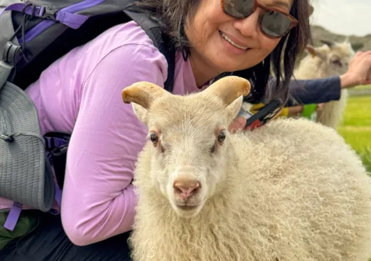 Woman wearing sunglasses, smiling behind a small goat