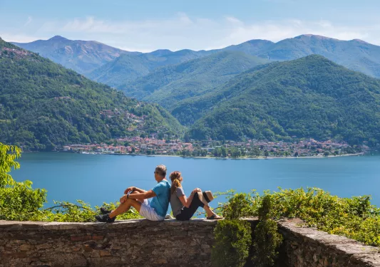 Man and woman sitting on a brick wall, looking out to a lake and a town in the distance