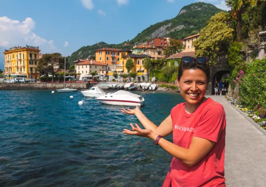 Woman smiling with her arms out, pointing towards docked boats