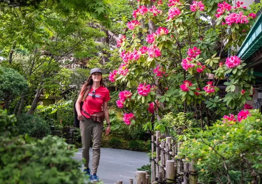 Woman smiling while walking through an outdoor garden full of plants and pink flowers