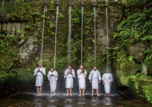People in white robes under an active waterfall