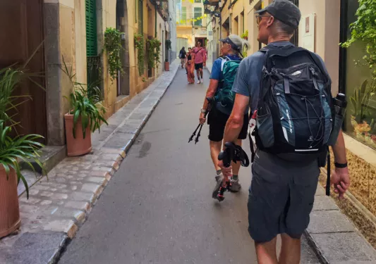 Group of men wearing backpacks, walking through a town alleyway with large buildings on either side
