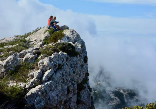 Man and woman sitting on a cliff, looking towards foggy valleys