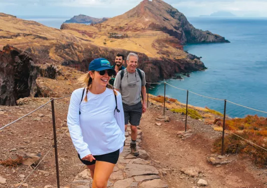 Woman and two men walking on a stone path on an island, with the ocean in the background