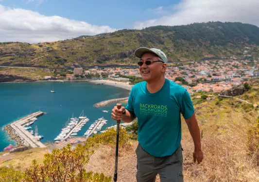 Man smiling while holding a hiking pole, with a town in the distance