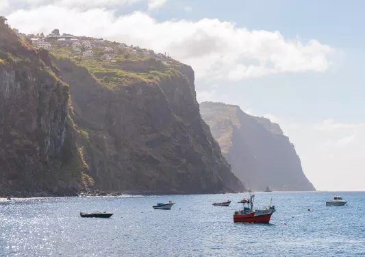 Boats floating in the ocean, with a large cliff with houses in the background