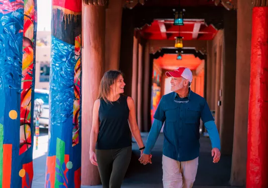Man and woman holding hands while walking in a colorful passage