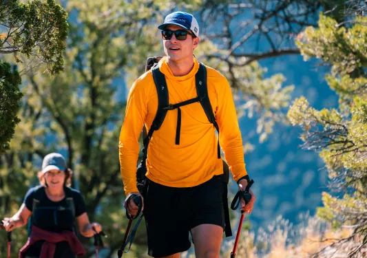 Man in an orange shirt with walking poles, ascending a rocky trail