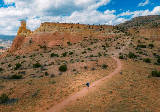 Top view of a man in blue ascending a dirt trail towards a mountain