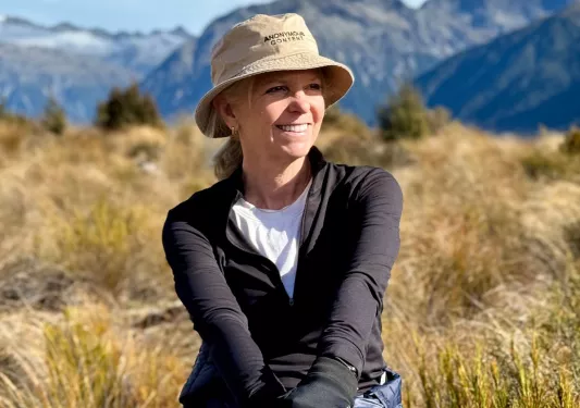Woman smiling in a field with large mountains ion the distance