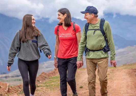 Two women and one man smiling while walking on a dirt trail