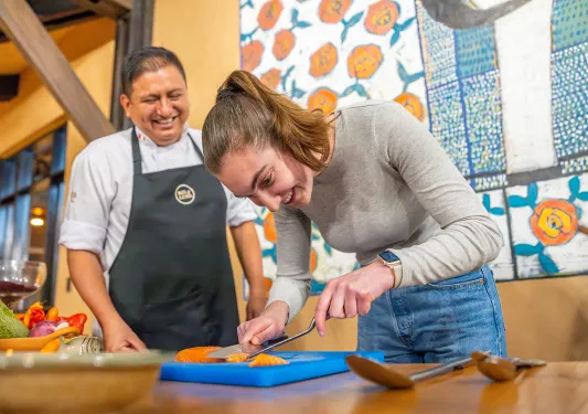 Woman cutting a piece of fish while a man is smiling behind her