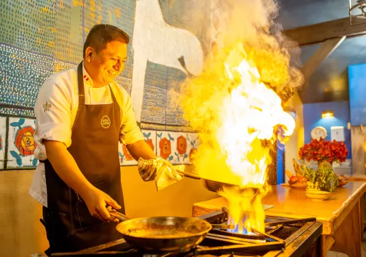 Man cooking with a flaming pot in his hand