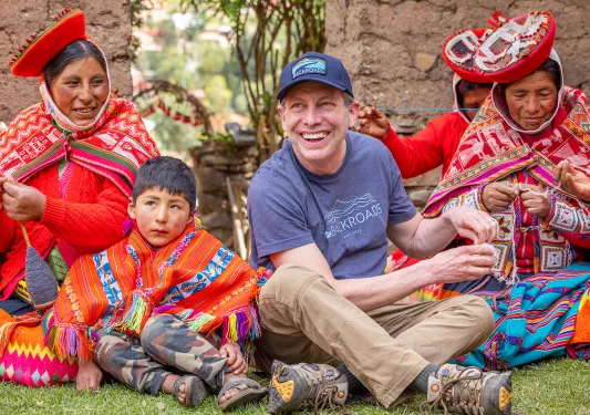 Man weaving items by hand with women in traditional attire
