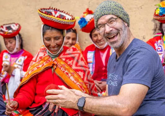 Man smiling while holding a ball of yarn, next to a woman wearing traditional attire