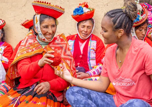 Woman in traditional attire handing another woman a ball of red yarn