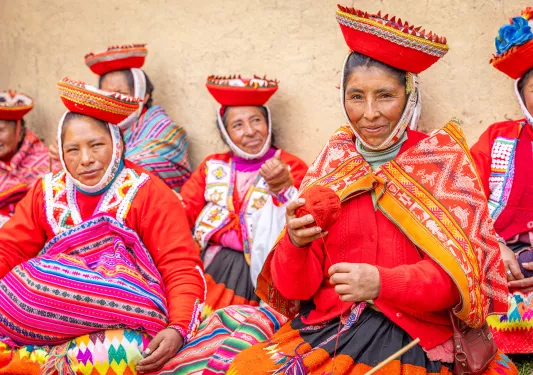 Group of women in traditional attire, holding red balls of yarn