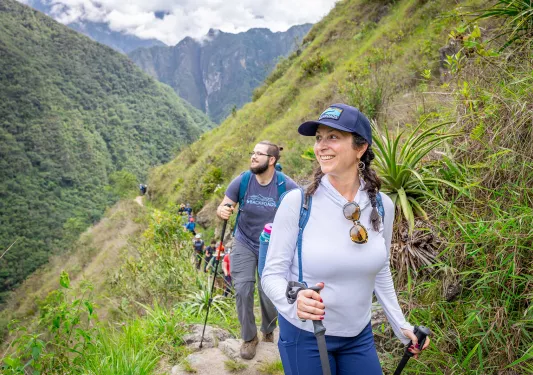 Woman and man walking on a dirt trail, smiling and looking out towards large hills