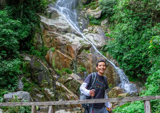 Man with a walking pole, walking across a wooden bridge with a small waterfall in the backgroun