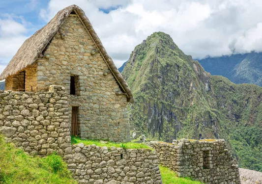 Rustic, stone buildings on top of a dirt trail with large mountains in the background