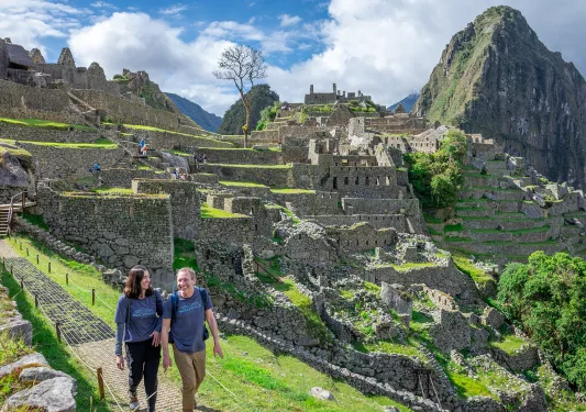 Man and woman smiling while walking on a stone path, with Machu Picchu in the background