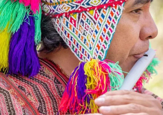 Person wearing traditional Peruvian attire, playing a flute