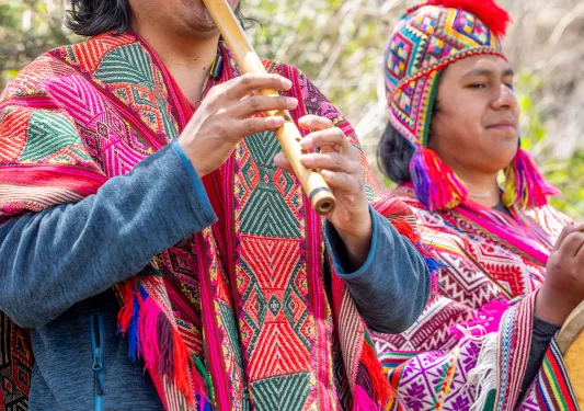 Two men with traditional attire, playing wooden flutes
