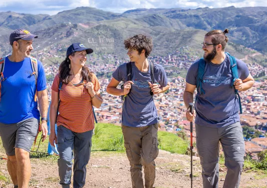 Group of 3 men and one woman ascending a dirt trail with a town in the distance