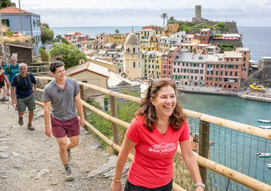 Group of people smiling while walking along a fenced, dirt trail with a town in the background