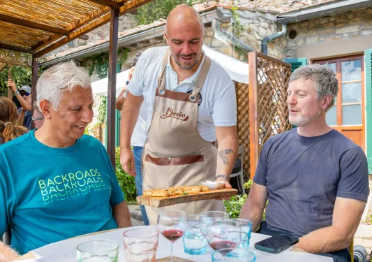 Waiter serving a wooden plank of food to two seated men