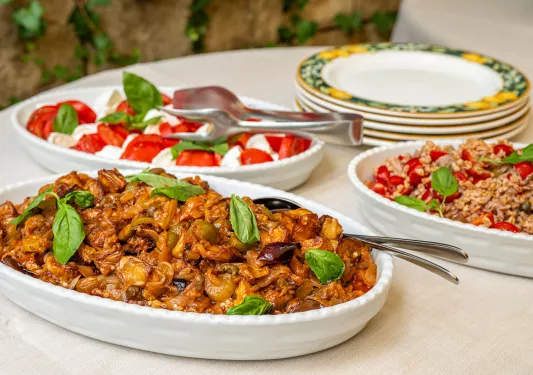 Three large baking dishes full of marinated meat and caprese salad