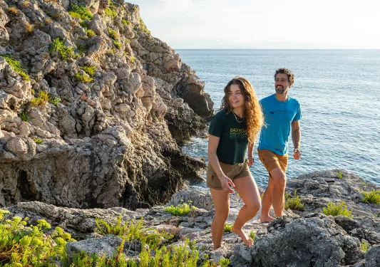 Man and woman walking on boulders next to the ocean shore