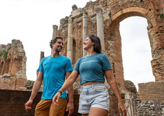 Man and woman smiling while looking at each other, with a large stone arch in the background
