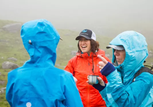 Women smiling while wearing rain jackets in the middle of a valley