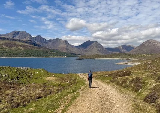 Person walking on a dirt trail towards a large lake