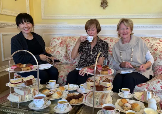 Group of three women sipping on tea and eating small pastries