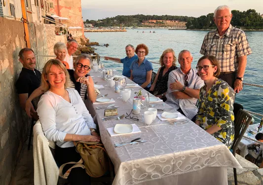 Group of people smiling, sitting around a dining table by the water