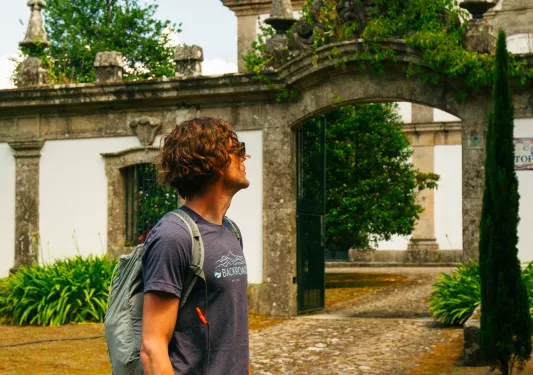 Man standing in front of a stone palace, surrounded by tall trees and bushes