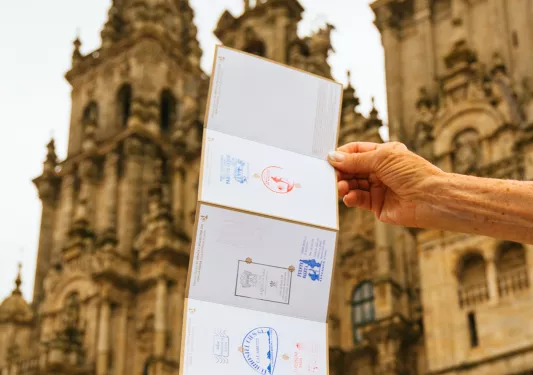 Person holding up a foldable stamp brochure in front of a large palace