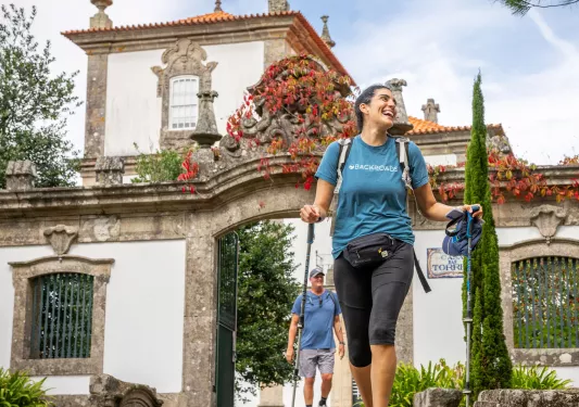 Woman smiling with two hiking poles, walking in front of a castle-like building