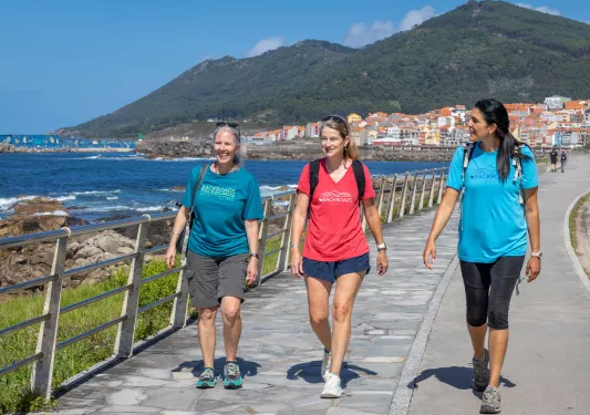 Three women walking on a stone path next to the ocean side