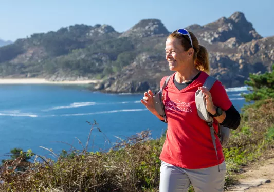 Woman wearing a red shirt, smiling while holding her backpack