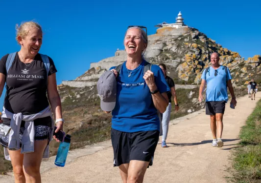 Group of men and women walking on a stone path with a large cliff in the background