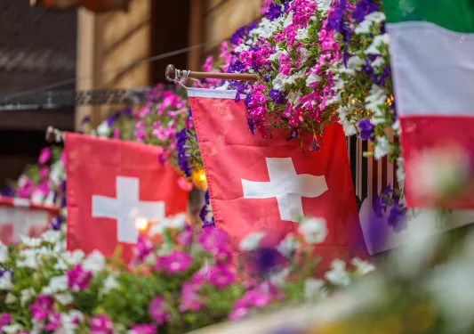 swiss flags hanging from a balcony with flowers