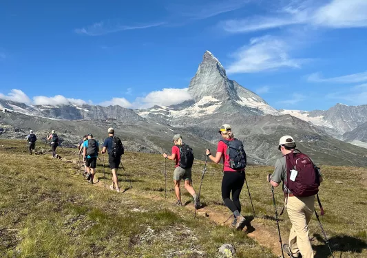 Group of people walking on a dirt trail, with large mountains in the distance