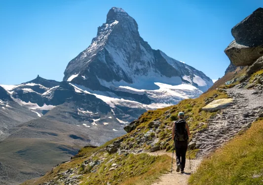 Woman using hiking poles, walking on a trail with tall mountains in front