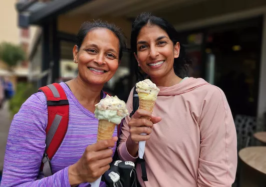 Two women holding up ice cream cones and smiling