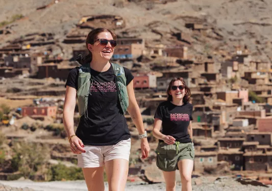 Two women smiling and walking with a town in the background
