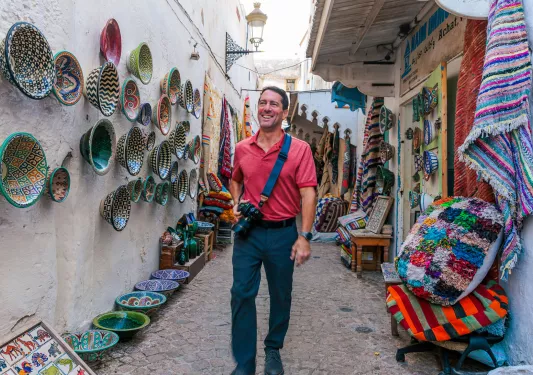 Man standing in an alleyway, surrounded by baskets and pots on the walls