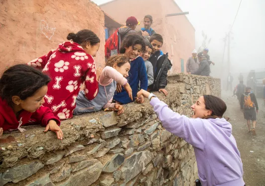 Woman smiling, reaching an arm out to a group of kids